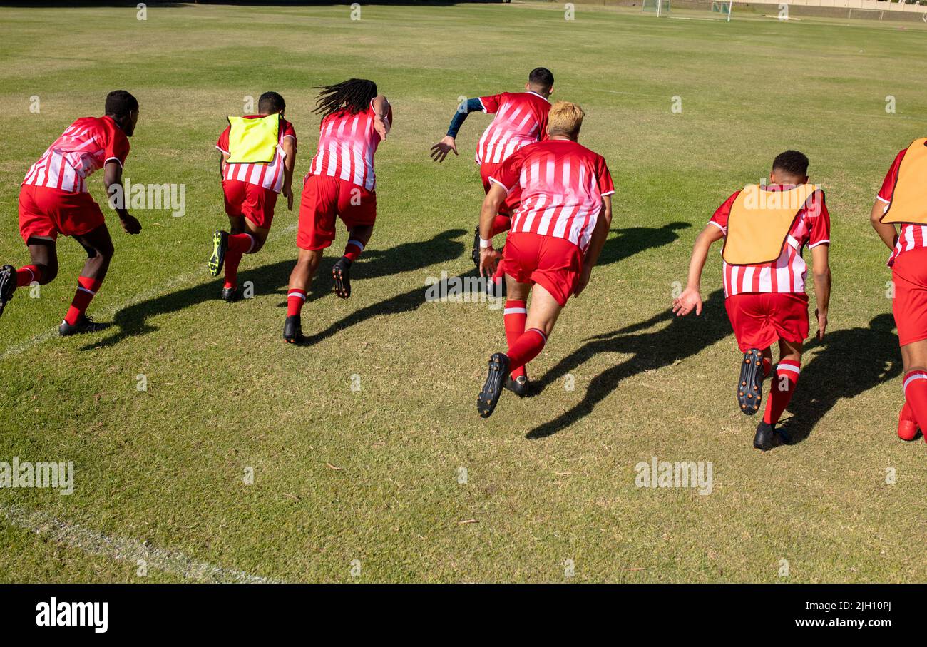 Vue en grand angle des joueurs masculins en uniforme rouge qui s'exécutent sur un terrain herbacé dans le terrain de jeu en été Banque D'Images