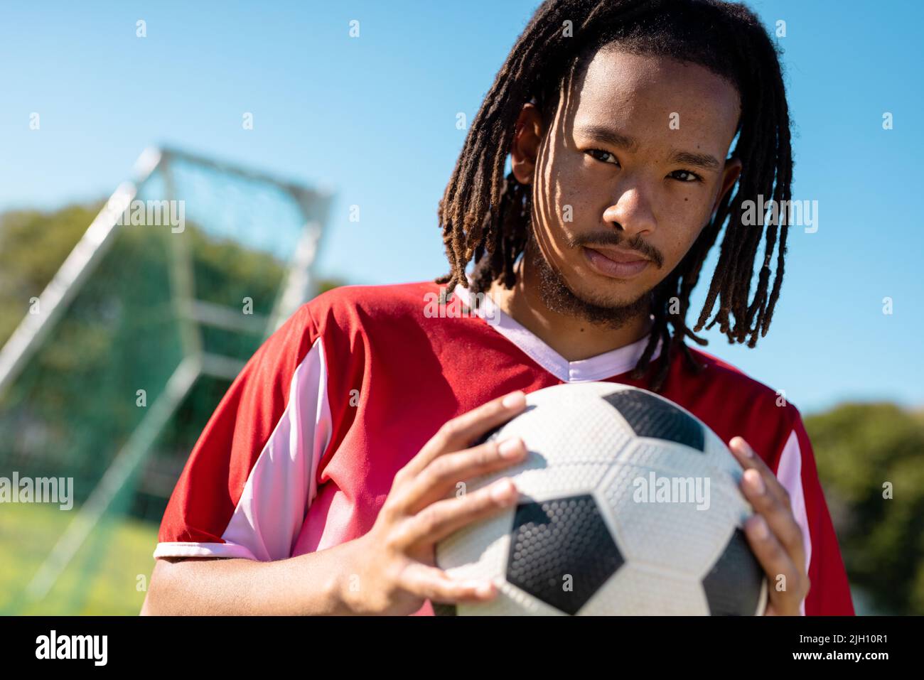 Portrait en bas angle d'un joueur masculin avec des dreadlocks en jersey rouge tenant le ballon contre le ciel clair Banque D'Images