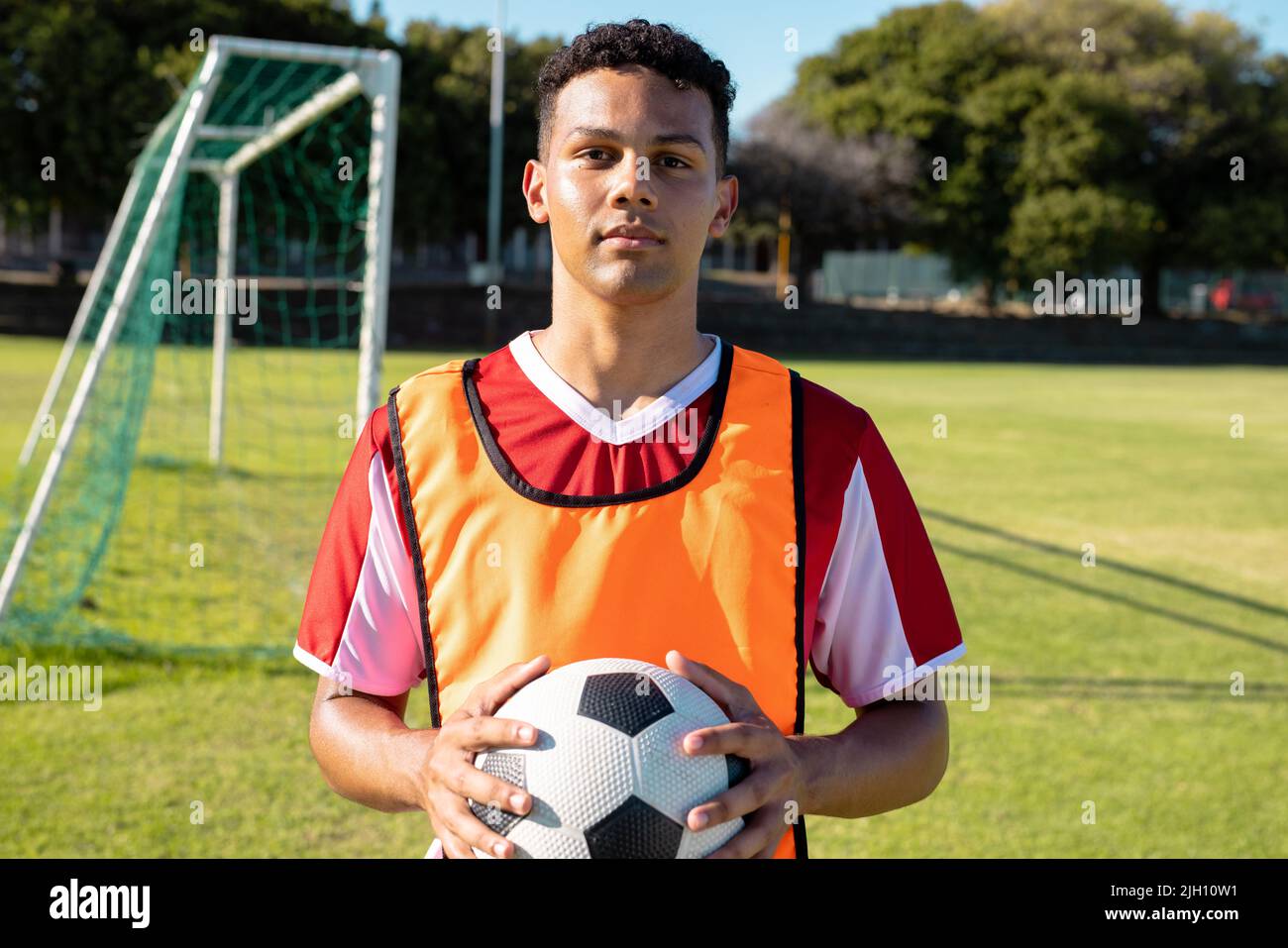 Portrait d'un athlète masculin confiant en uniforme de football tenant le ballon tout en étant debout dans le terrain de jeu Banque D'Images