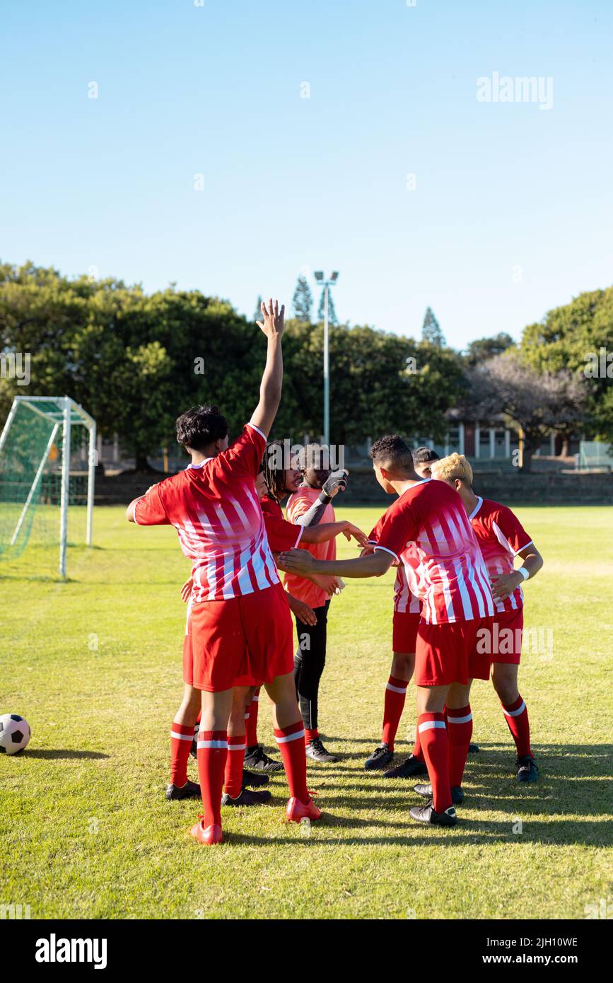 Joueurs multiraciaux hommes en uniforme levant les mains avant le match contre le ciel clair à l'aire de jeux Banque D'Images