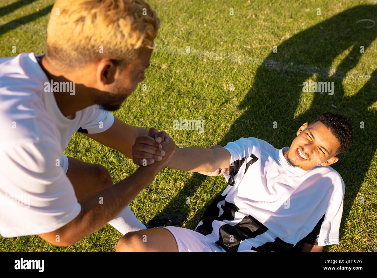 Vue en grand angle d'un joueur caucasien qui aide un coéquipier blessé allongé sur le terrain à se lever Banque D'Images