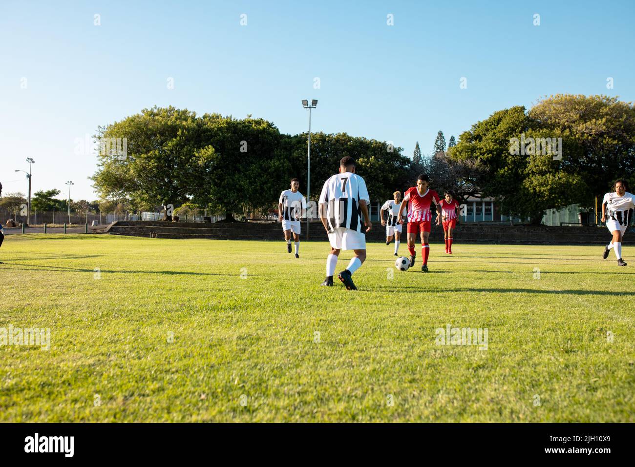 Des équipes multiraciales de sexe masculin jouent à un match de football dans un terrain de jeu dans un ciel dégagé, par beau temps, dans un espace de copie Banque D'Images