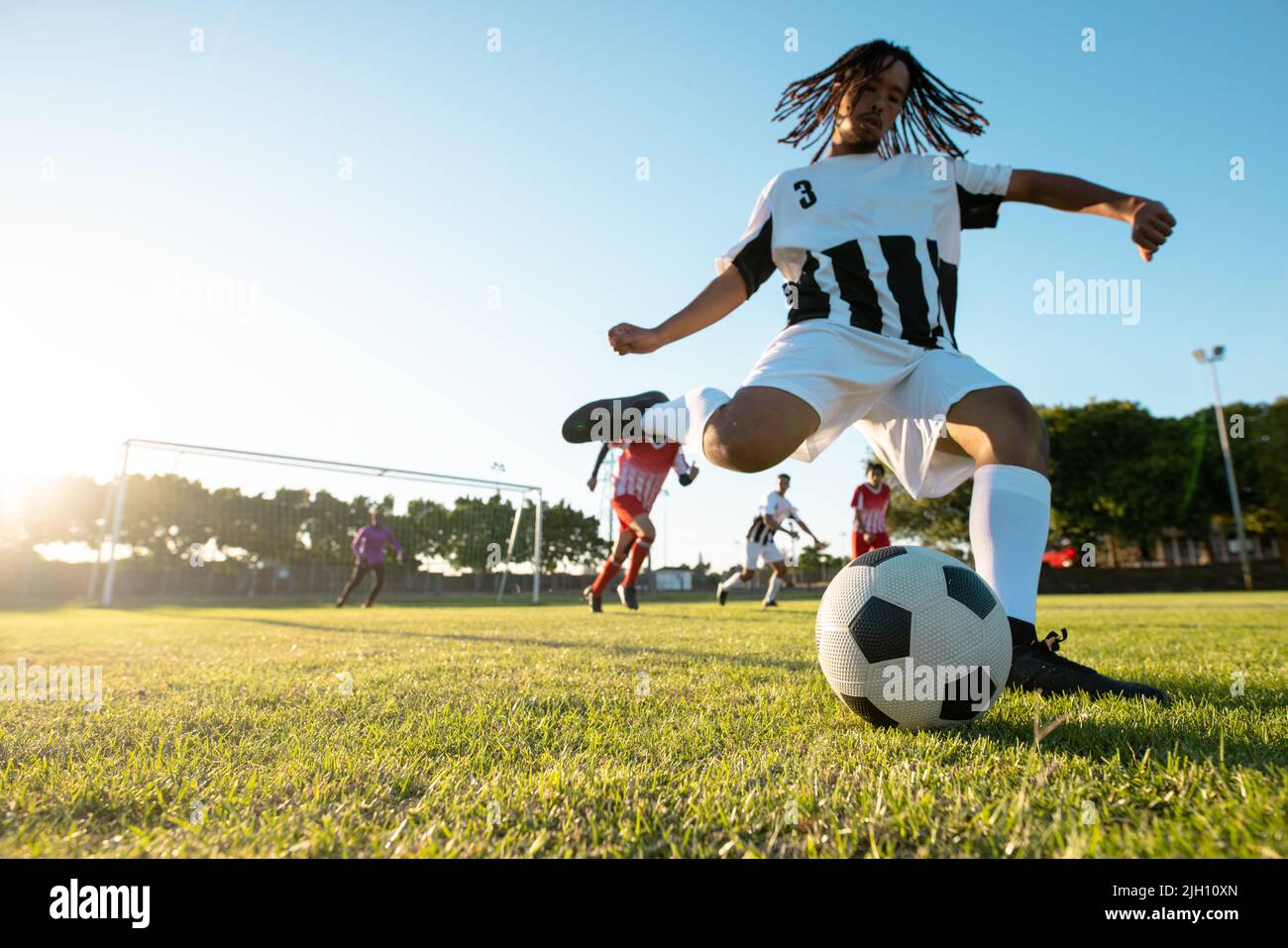 Vue en contre-plongée du joueur multiracial qui joue au ballon lors d'un match de football contre un ciel dégagé Banque D'Images