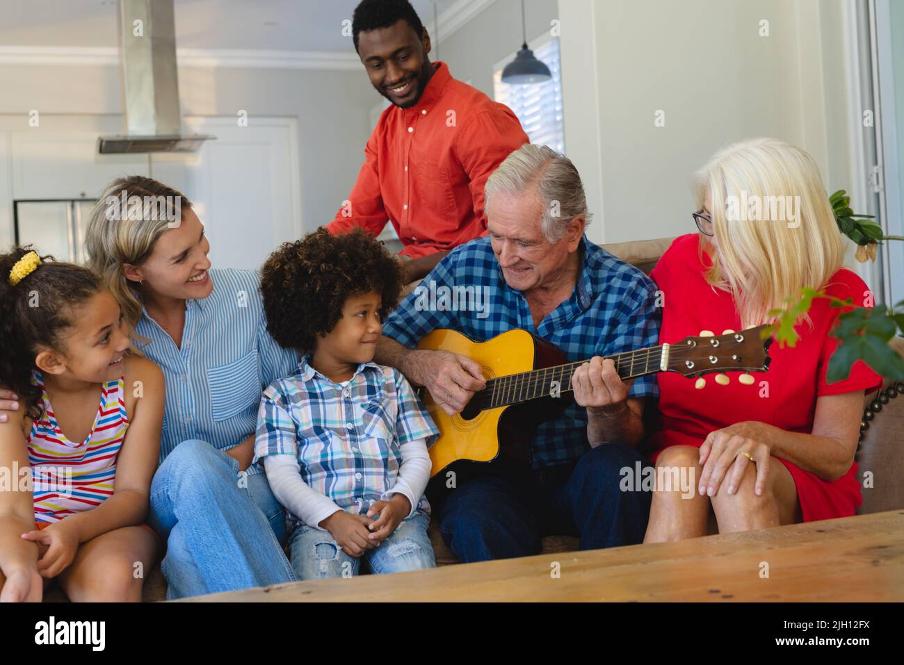 Bonne famille multiraciale multigénération regardant un homme senior jouant de la guitare tout en étant assis sur un canapé Banque D'Images