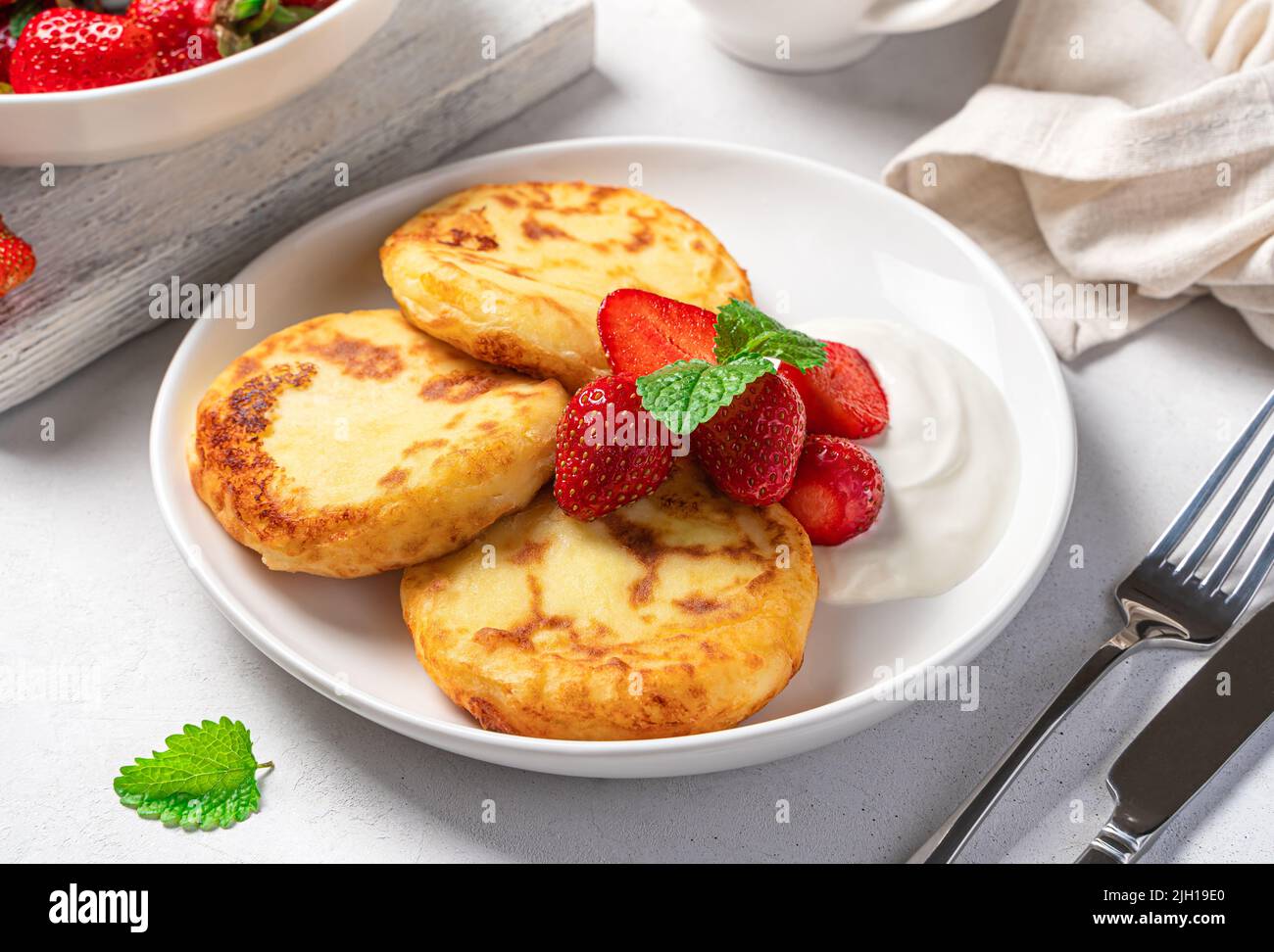 Crêpes au fromage cottage avec fraises, menthe et crème sure dans une assiette blanche sur fond gris. Banque D'Images