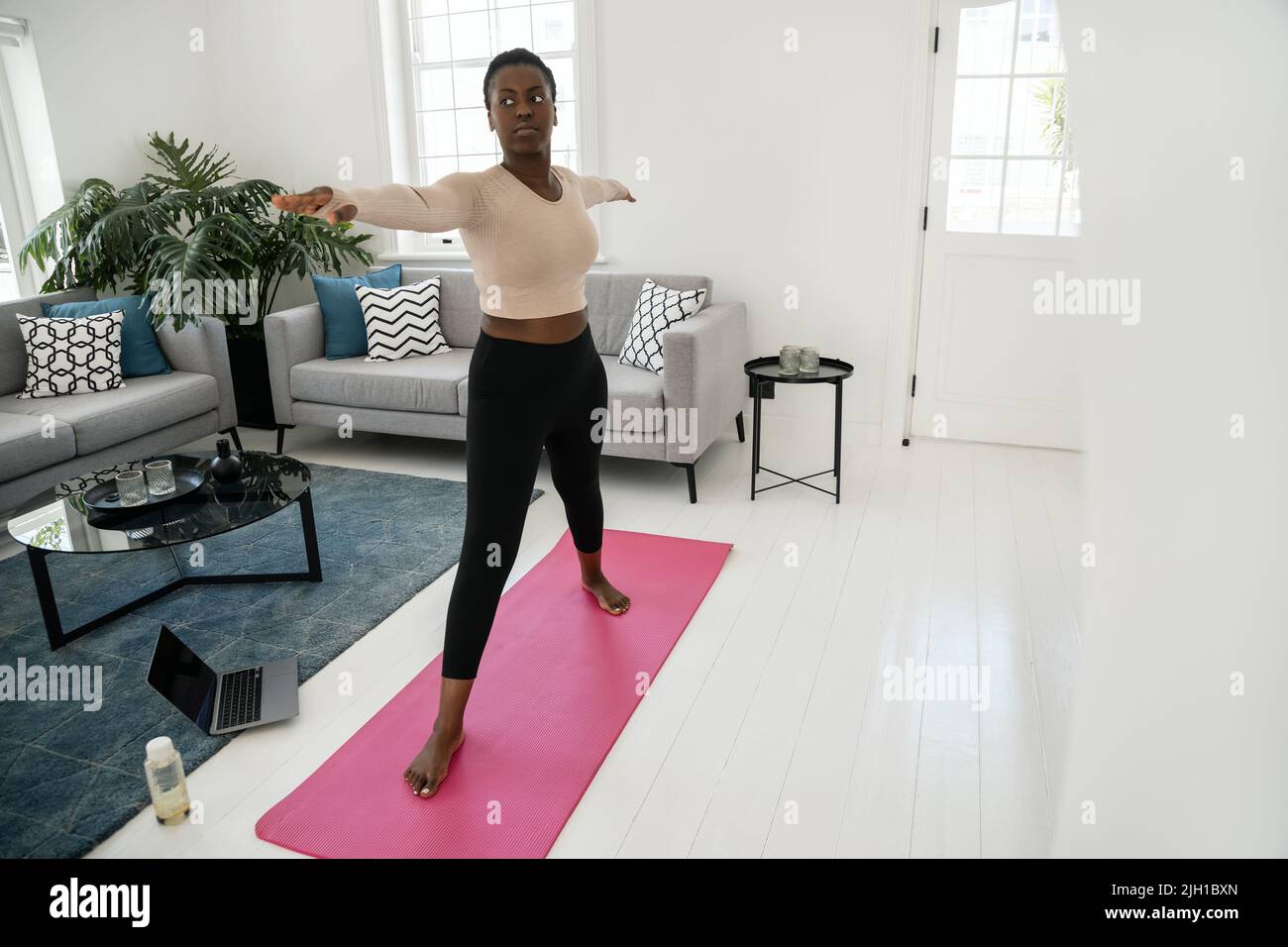 Jeune femme africaine noire s'étirant dans la posture du yoga guerrier, suivant un cours de fitness en ligne. Faites de l'exercice dans le salon moderne de la maison Banque D'Images