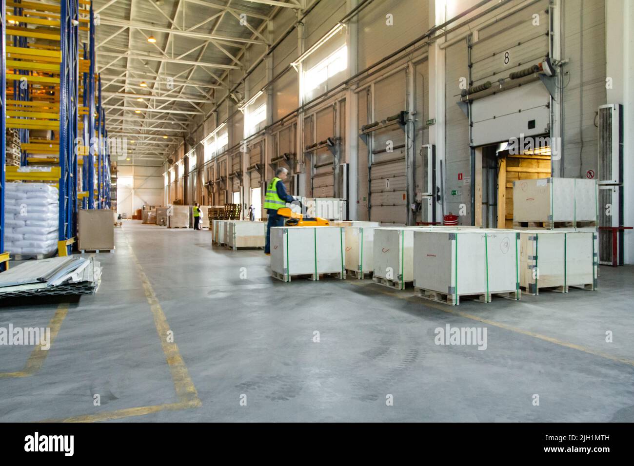 Intérieur d'un entrepôt moderne de stockage de magasin de détail avec transpalette près des étagères et des rampes de chargement. Ouvrier de magasin en uniforme travaillant sur des forkli Banque D'Images Intérieur d'un entrepôt moderne de stockage de magasin de détail avec transpalette près des étagères et des rampes de chargement. Ouvrier de magasin en uniforme travaillant sur des forkli Banque D'Images