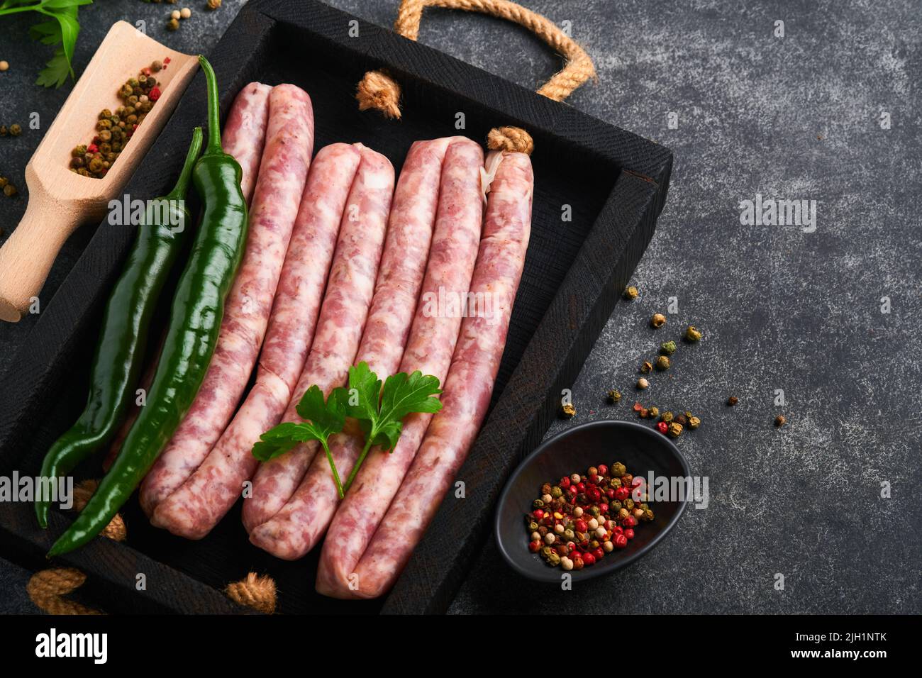 Saucisses crues. Bratwurst ou saucisses avec ingrédients sur planche à découper avec épices sur fond de pierre avec espace de copie. Cuisine de fond. Haut Banque D'Images