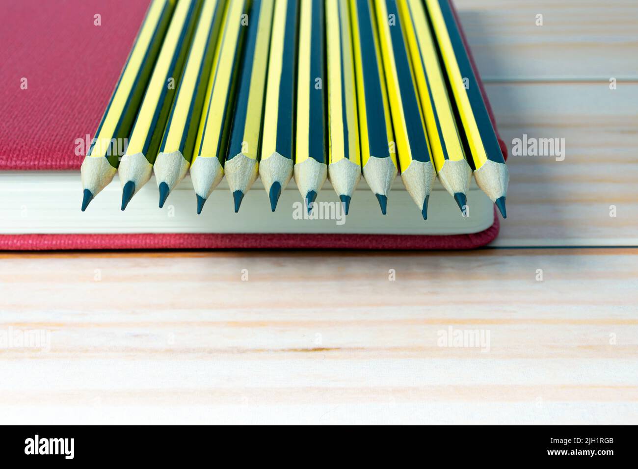 2b crayons en bois, sur une table en bois, posés sur un livre rouge. Copier l'espace. Banque D'Images