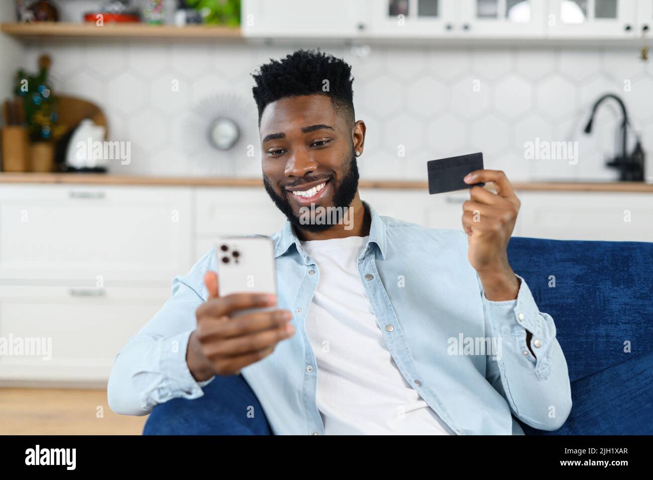 Transaction en ligne, paiement. Homme multiracial tenant une carte de crédit et utilisant un smartphone pour faire des achats, un gars à la peau sombre avec téléphone mobile et faire des achats en ligne Banque D'Images