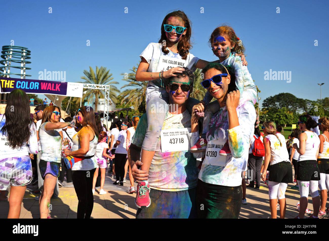 Une famille heureuse et souriante pose pour une photo à la Color Walk à Dubaï, aux Émirats arabes Unis. Les parents ont les deux filles sur le pigegyback. Événement en plein air amusant. Banque D'Images
