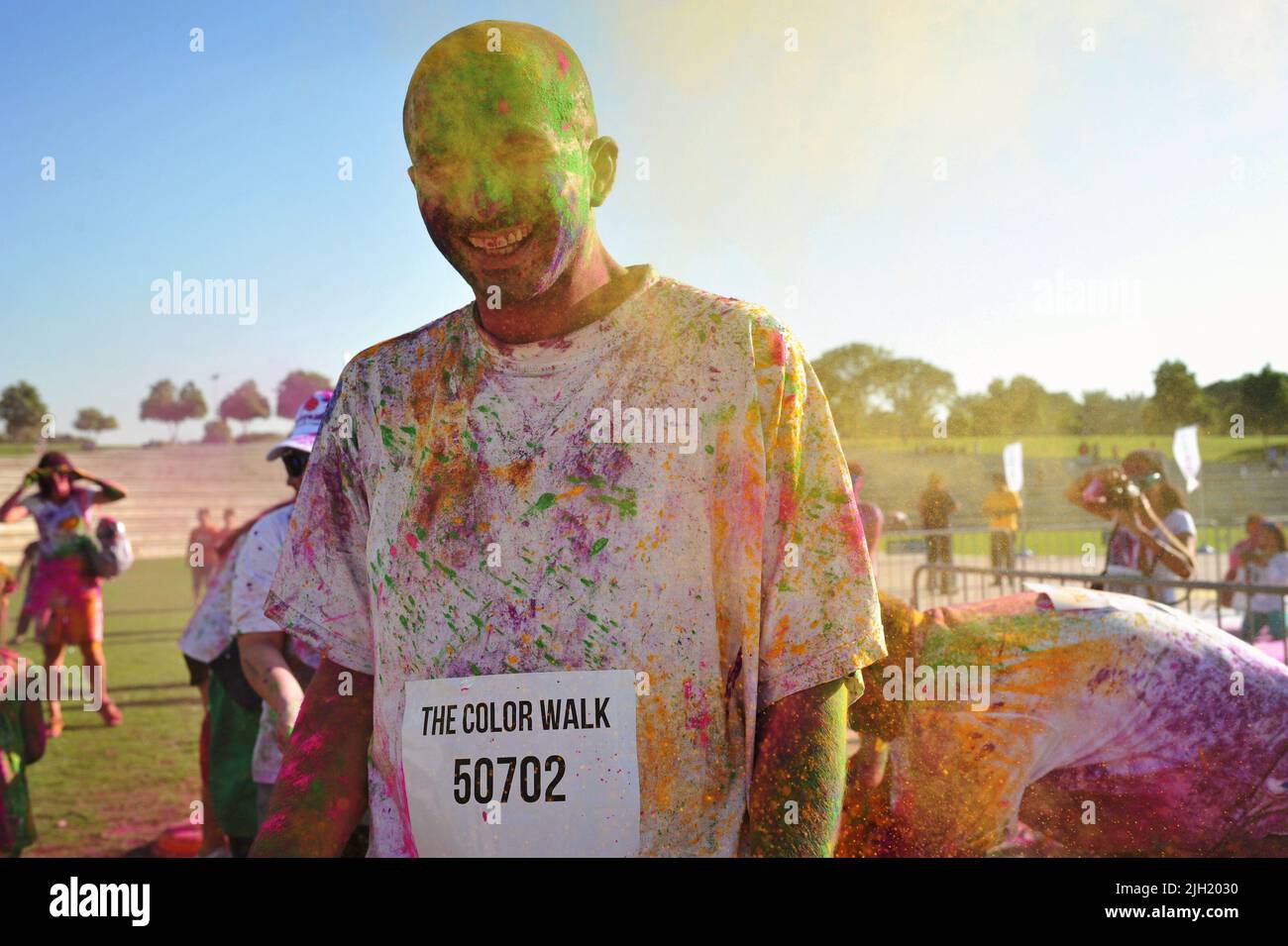 L'homme adulte rit alors qu'un groupe de personnes lance de la poudre colorée autour de lui lors d'une Color Walk à Dubaï, aux Émirats arabes Unis. Parc d'été extérieur amusant. Banque D'Images