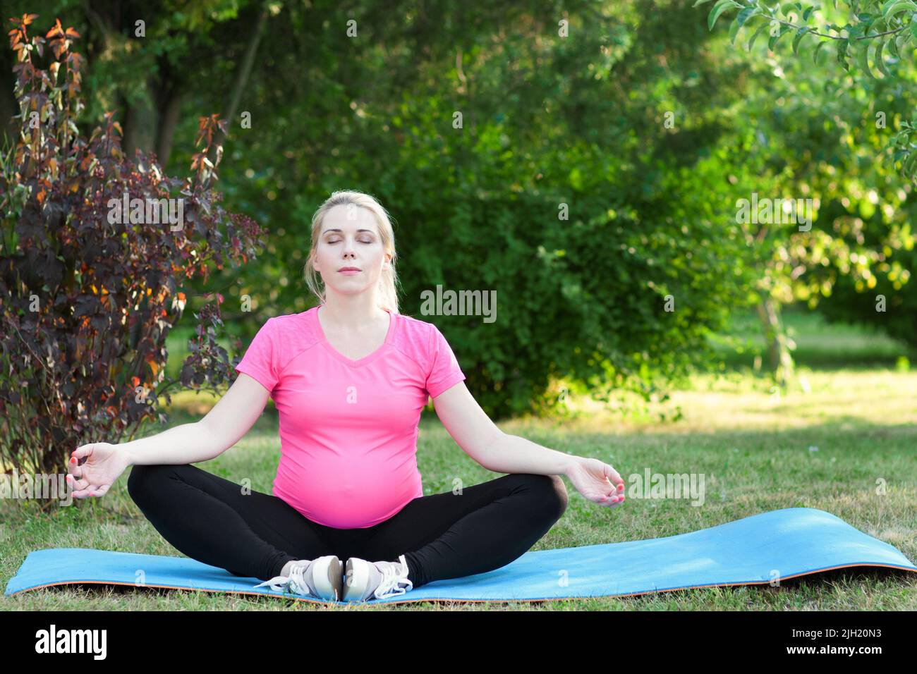 Jolie femme enceinte pratiquant le yoga en plein air Banque D'Images