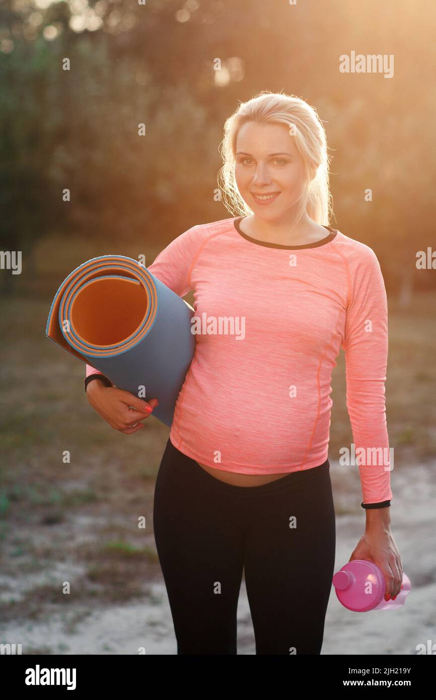 Femme enceinte souriant à l'appareil photo, lumière du soleil Banque D'Images
