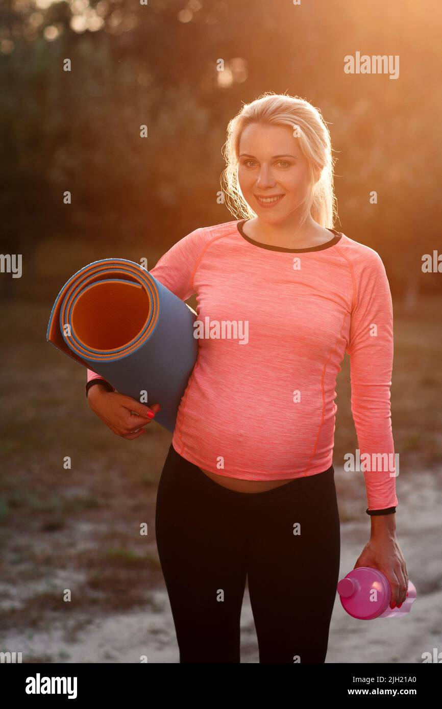 Femme enceinte souriant à l'appareil photo, lumière du soleil Banque D'Images
