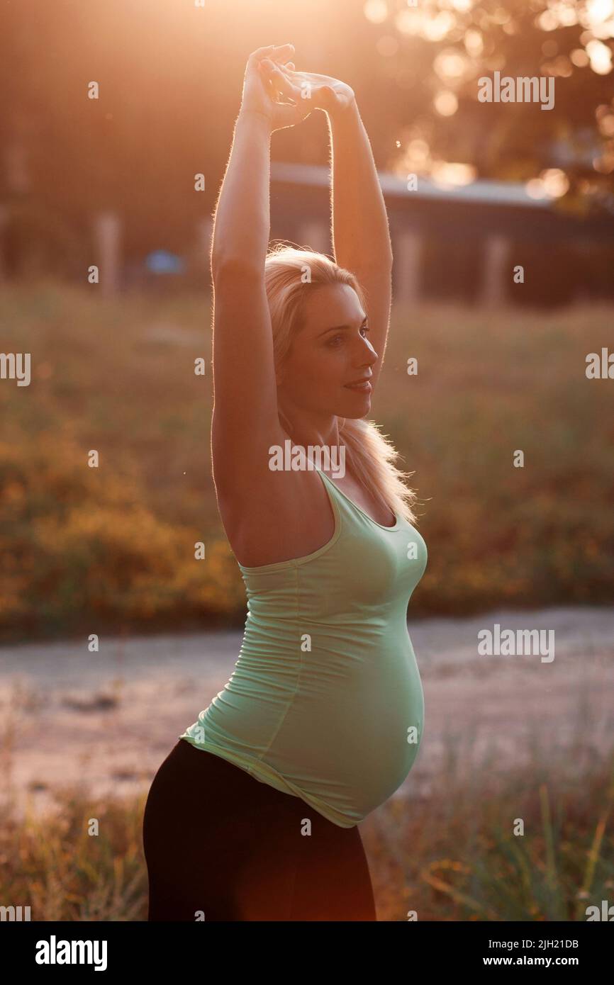 Bonne femme enceinte s'étirant à l'extérieur, lumière du soleil Banque D'Images