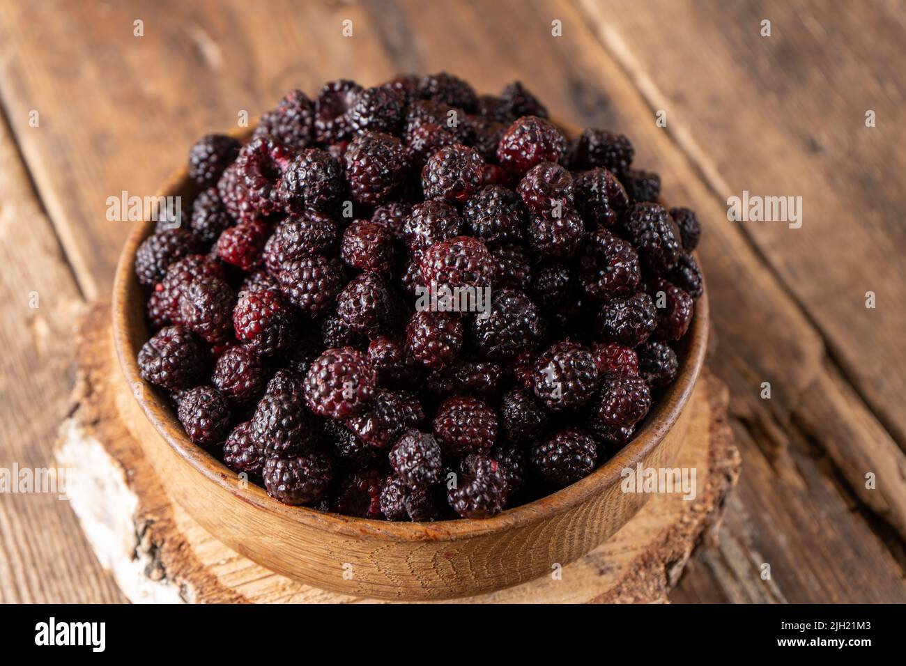 La baie noire est un hybride de framboises et de mûres. Baies dans un bol en bois sur la table. Vitamine nourriture d'été. Récolte. Raspberry et blackberry. Framboise noire. Banque D'Images
