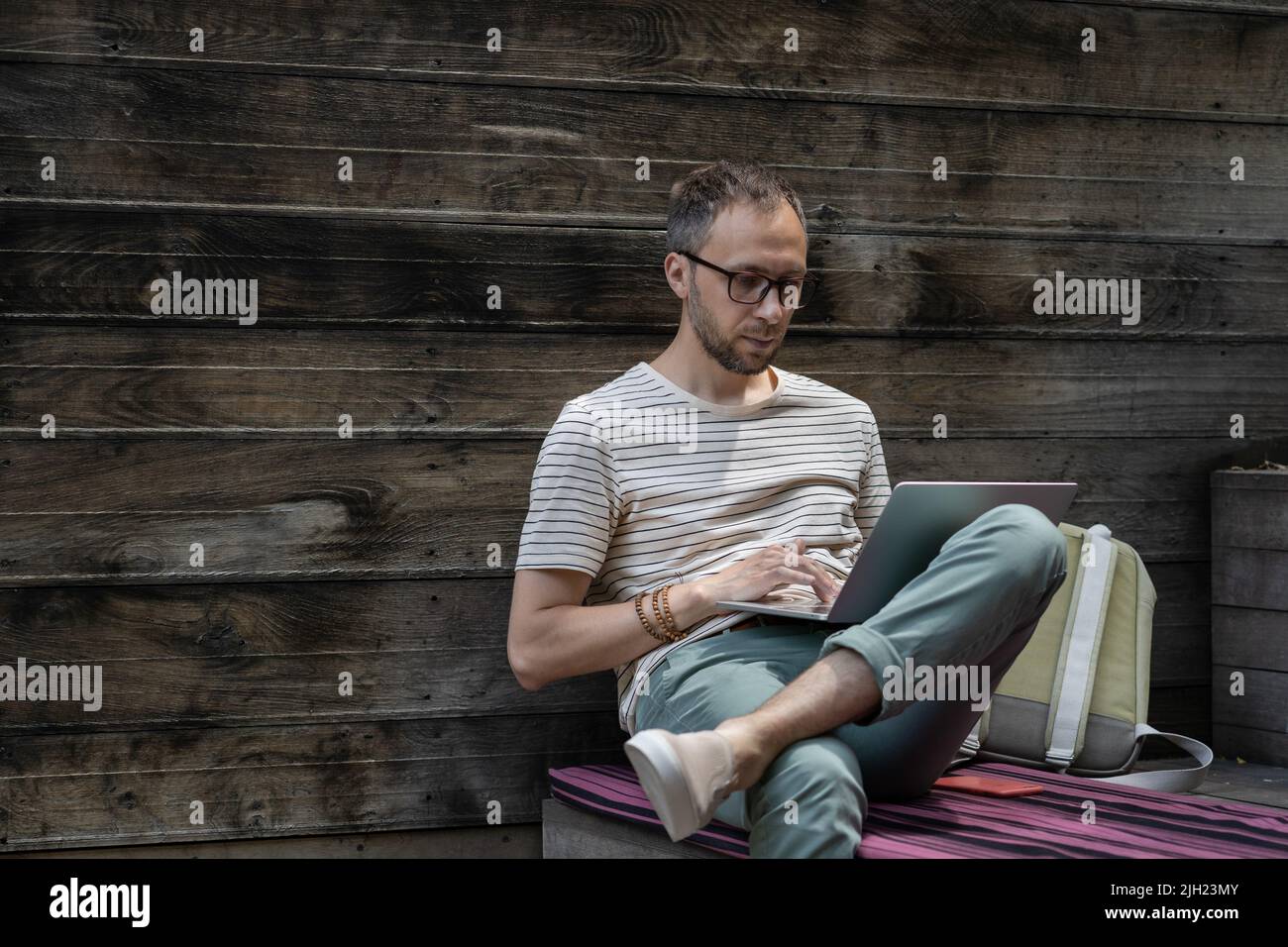 Jeune homme concentré portant des lunettes utilisant un ordinateur portable, dactylographiant sur le clavier, indépendant travaillant en ligne Banque D'Images