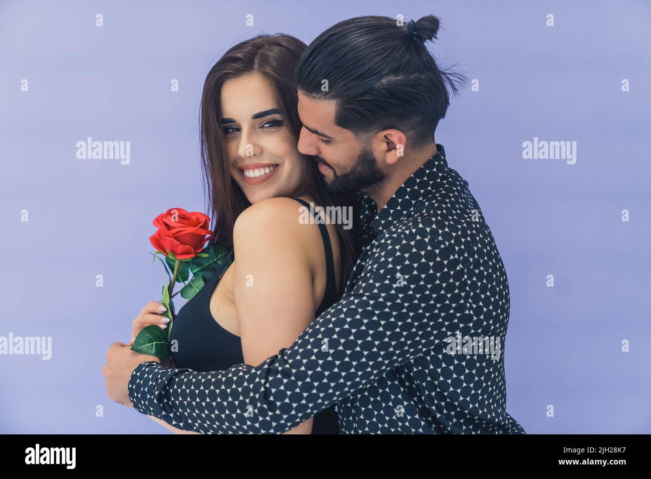 Surprise de fleur. Beau cubain à poil sombre embrassant sa jeune femme bien-aimée du dos et lui donnant une belle rose rouge. . Photo de haute qualité Banque D'Images