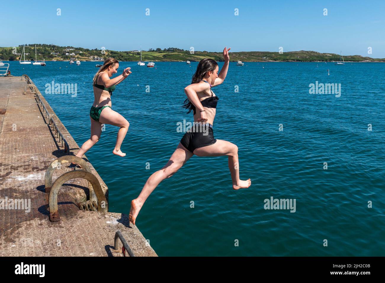 Schull, West Cork, Irlande. 14th juillet 2022. Les températures à West Cork ont atteint 23C aujourd'hui, avec de nombreuses personnes se dirigeant vers la côte pour se rafraîchir. Amelia Davies de Durrus et Amy Wilde de de Schull sautent de l'embarcadère pour se rafraîchir. Crédit : AG News/Alay Live News Banque D'Images