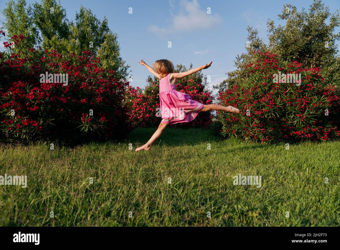Une fille saute dans le parc sur l'herbe près des buissons de la lauriers-roses. Banque D'Images