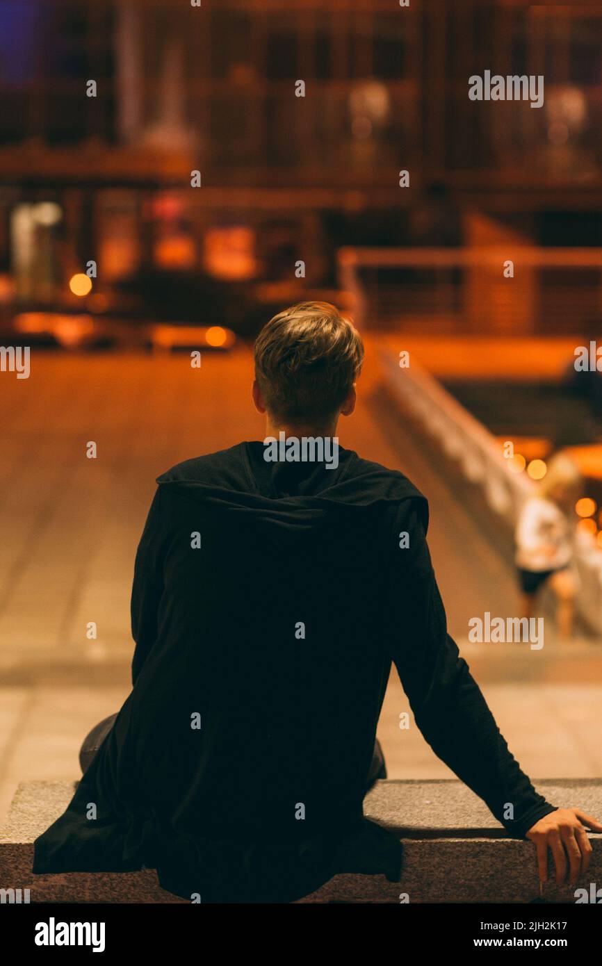 Homme assis dans la rue de nuit, vue arrière Banque D'Images