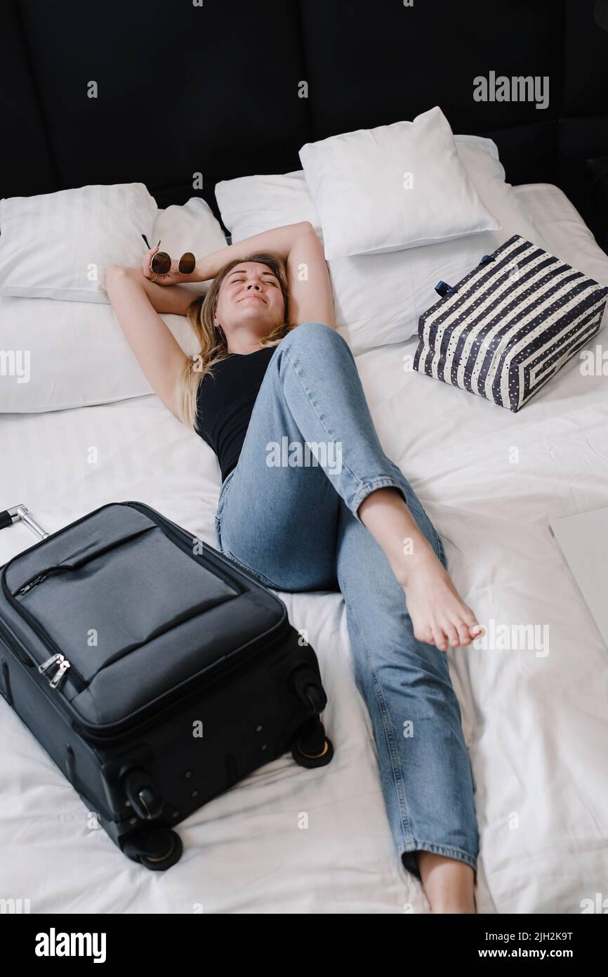 Femme avec une valise sur le lit dans l'hôtel ayant le repos pendant le voyage. Happy Traveler décontracté avec des sacs dans l'auberge vue de dessus. Profiter de la réservation de voyage appartements Banque D'Images