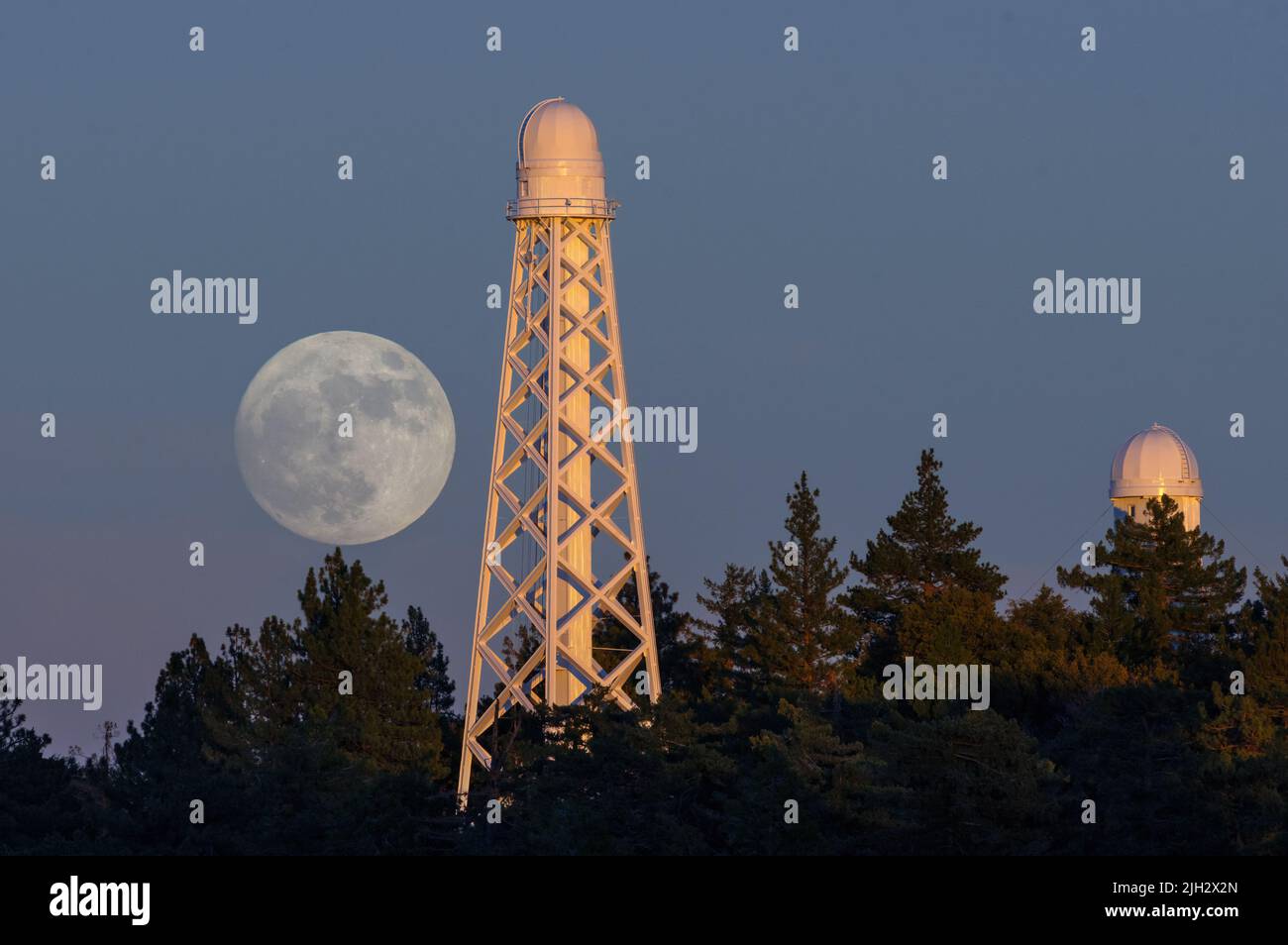 Vue sur une montée en lune depuis l'observatoire de Mt Wilson dans le comté de Los Angeles, présentée contre le télescope solaire de 150 mètres au milieu des pins. Banque D'Images