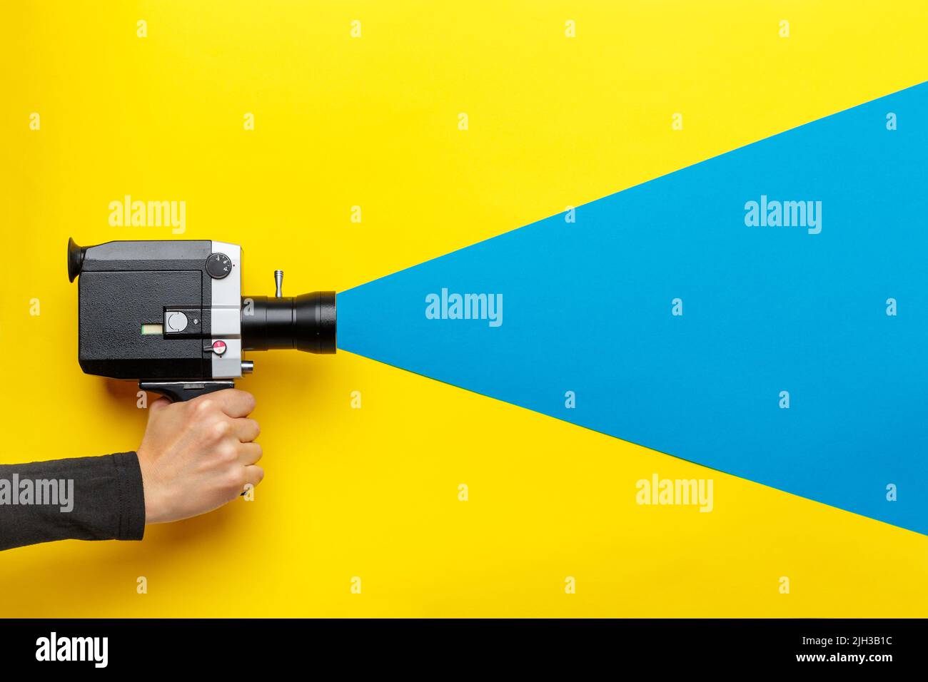 Main féminine tenant un ancien caméscope sur fond jaune avec un rayon bleu sortant de l'appareil photo, imitant le processus de prise de vue. Film makin Banque D'Images