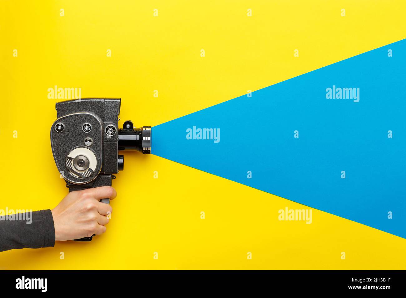 Main féminine tenant un ancien caméscope sur fond jaune avec un rayon bleu sortant de l'appareil photo, imitant le processus de prise de vue. Film makin Banque D'Images