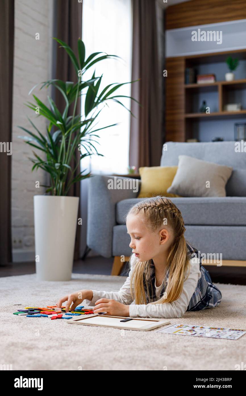 Jouets éducatifs pour enfants. Jolie petite fille faisant un puzzle en bois avec des blocs colorés sur la moquette à la maison. Jouet pour casse-tête pour moteur Banque D'Images