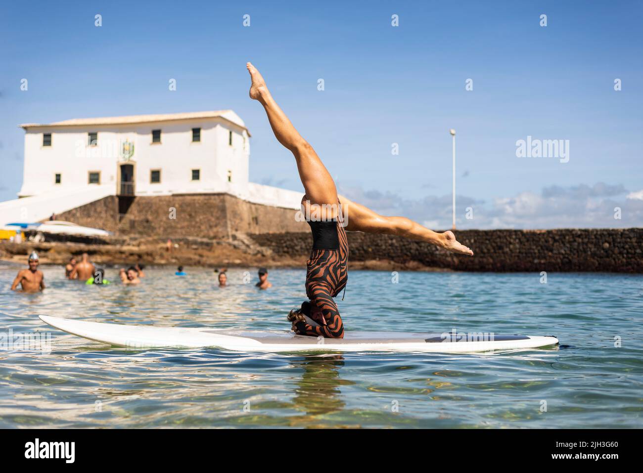 Une femme se dresse à l'envers sur une planche de surf à la plage de Porto da Barra à Salvador, Bahia. Banque D'Images