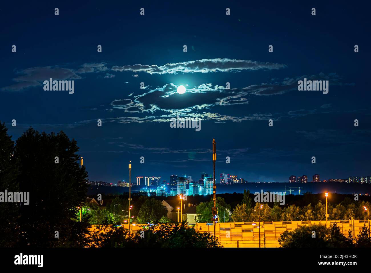 Ciel spectaculaire coloré avec pleine lune et nuages, nuit sombre de la ville en été, éclairage du bâtiment Banque D'Images