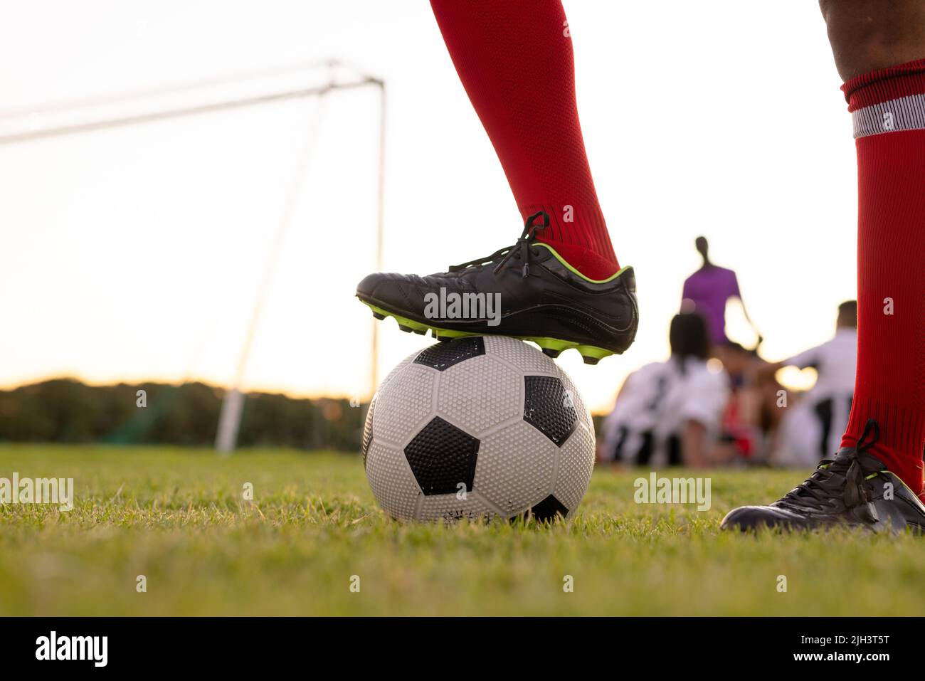 Coupe basse d'athlète de sexe caucasien portant des chaussettes rouges et des chaussures noires mettant la jambe sur le ballon de football Banque D'Images