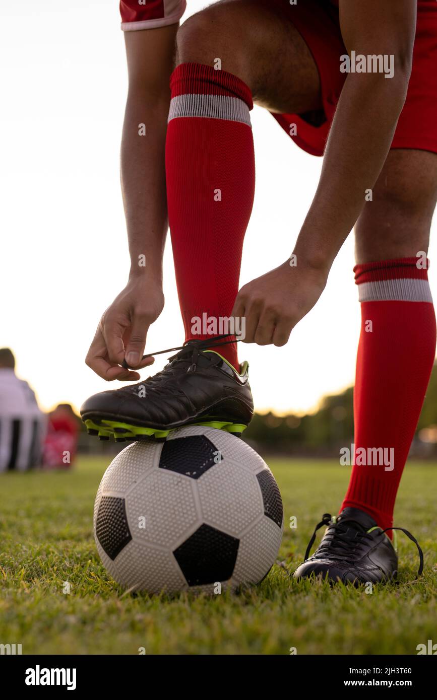 Coupe basse d'athlète de sexe masculin caucasien portant des chaussettes rouges avec une jambe sur le ballon de football nouant le lacet Banque D'Images