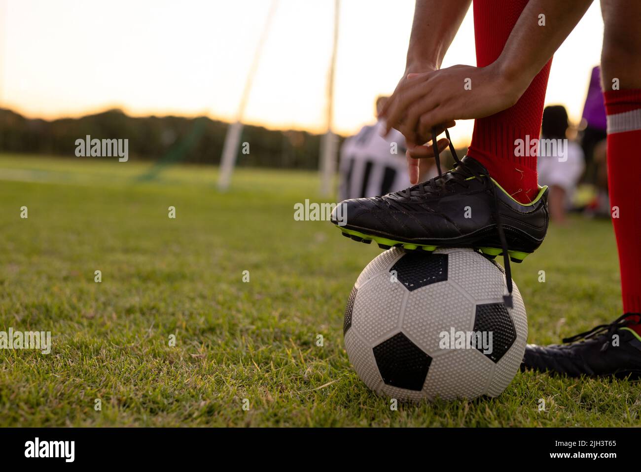 Coupe basse d'un homme caucasien portant des chaussettes rouges avec une jambe sur le ballon de football nouant le cordonnet Banque D'Images