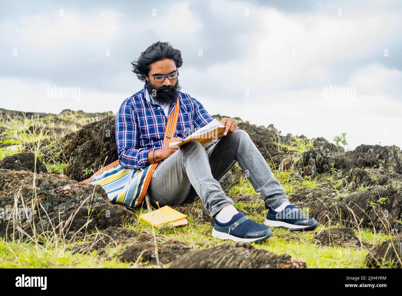 Un auteur de barbe réfléchi écrit sérieusement un roman tout en étant assis au sommet de la colline - adepte de l'artiste, de la créativité et de l'imagination. Banque D'Images