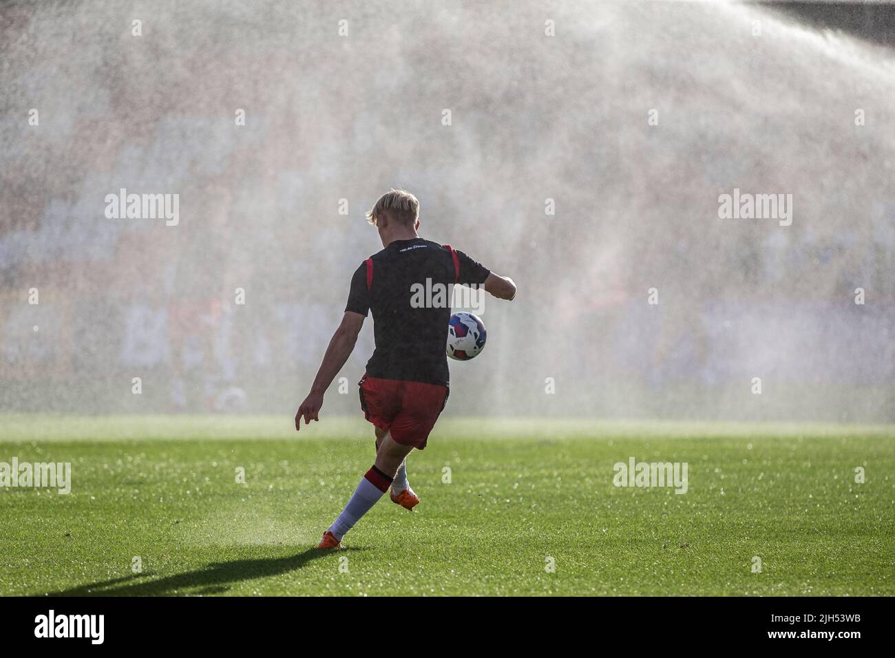 Le football se réchauffe avant un match de ligue inférieure tandis que les arroseurs vaporisent de l'eau. Banque D'Images