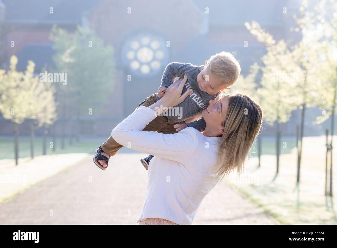 une jeune et heureuse mère et enfant, jouant, se tient au milieu d'un parc dans les rayons du soleil levant du matin. Photo de haute qualité Banque D'Images