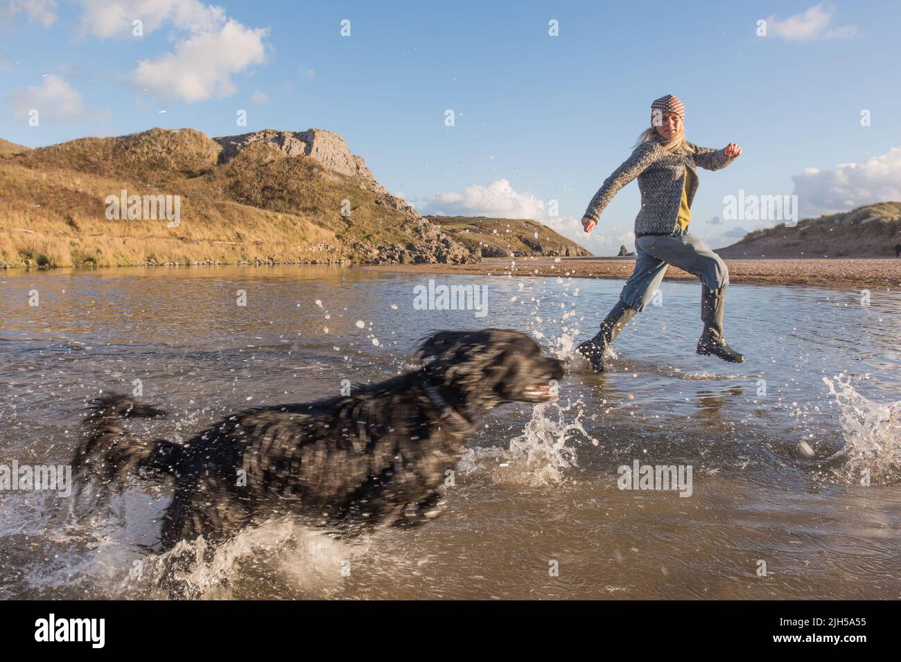 Femme en train de courir avec un chien dans un lagon, large Haven South Beach, Pembrokeshire Coast National Park, pays de Galles, Royaume-Uni Banque D'Images