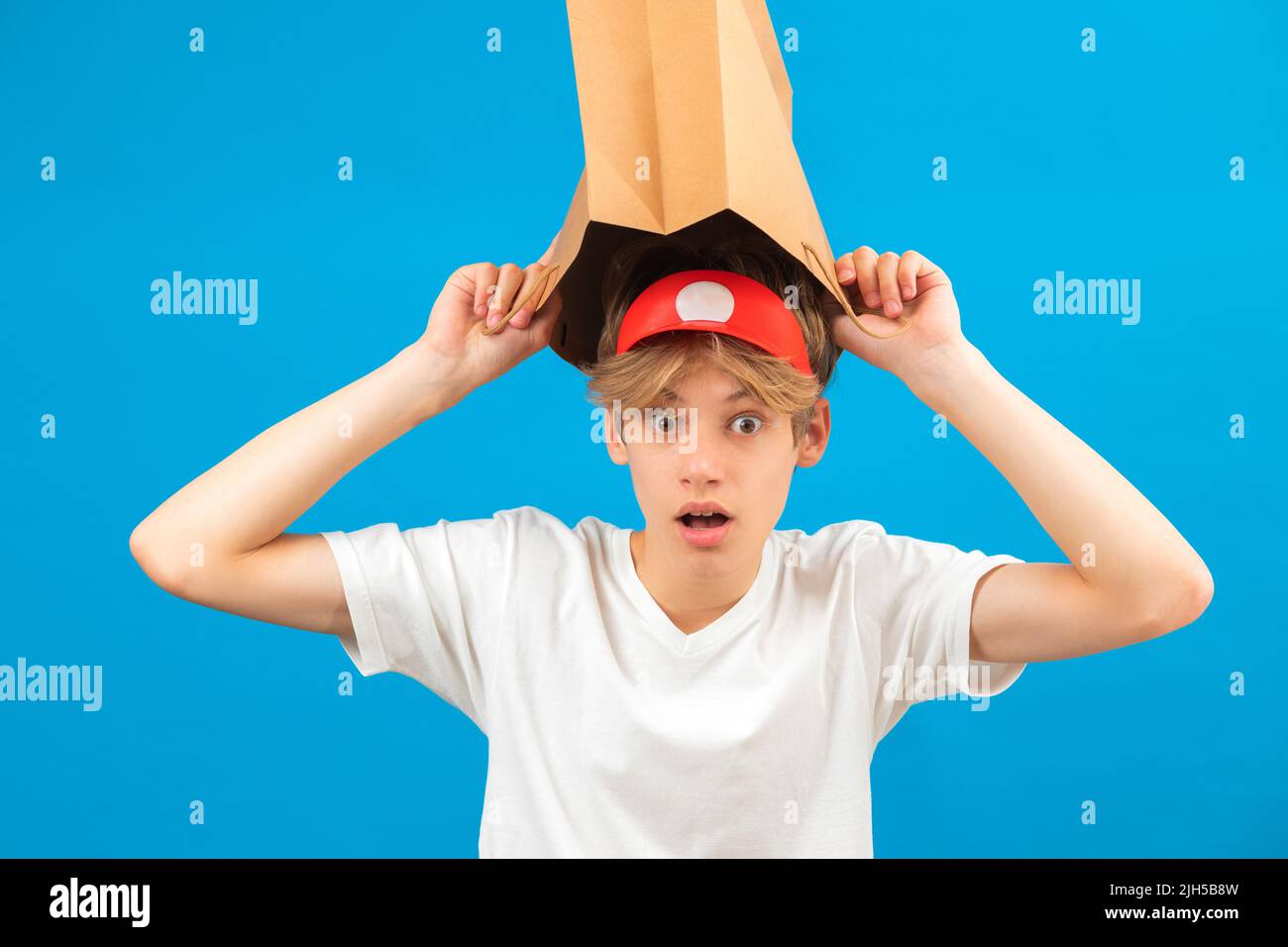 Un jeune garçon choqué avec un sac en papier sur la tête. Adolescent tenant un sac de papier au-dessus de la tête posant en studio. Banque D'Images