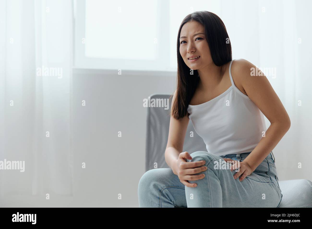 Crampes orteil cassé os cassé dans la jambe. Souffrance tourmentée bronzée belle jeune femme asiatique touche la jambe à la maison intérieur salon. Blessures faibles Banque D'Images