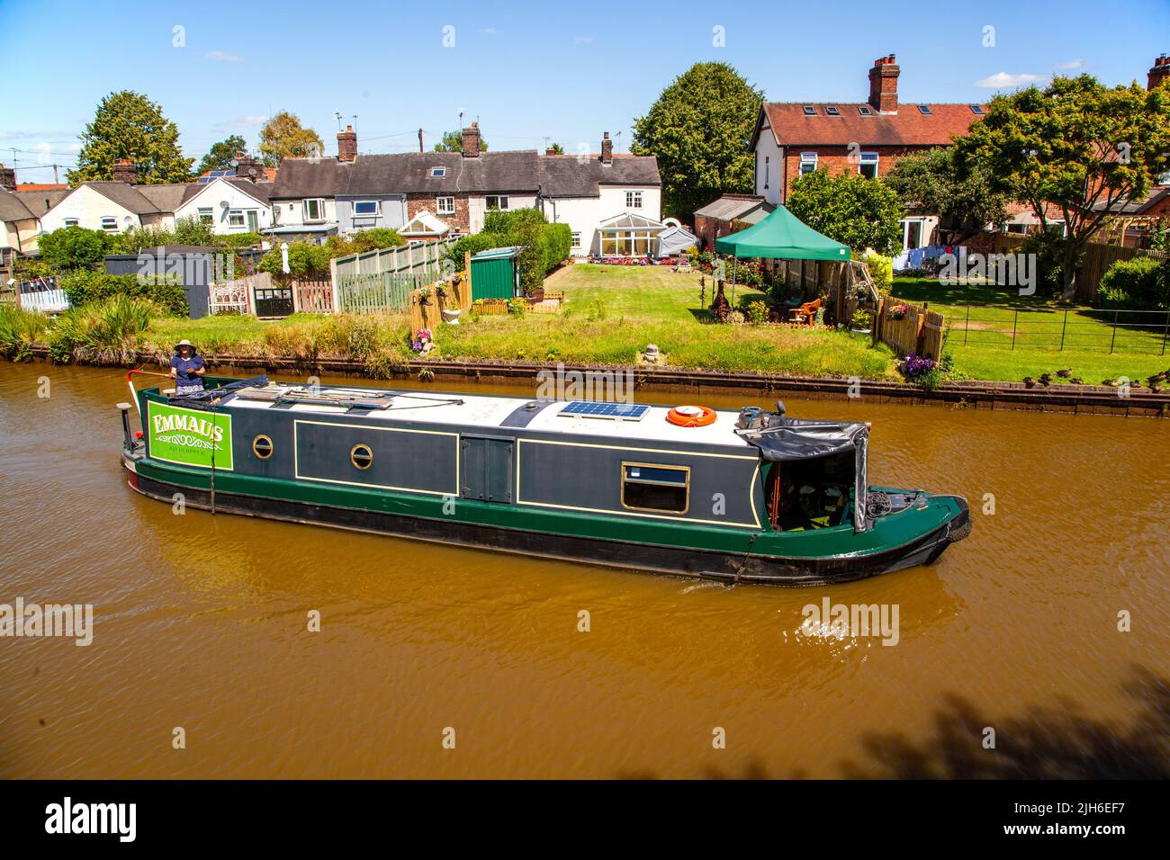 Les gens sur un canal narrowboat vacances en passant par des chalets du côté du canal à l'approche de l'écluse 63 à Malkins Bank Cheshire sur le canal Trent et Mersey Banque D'Images