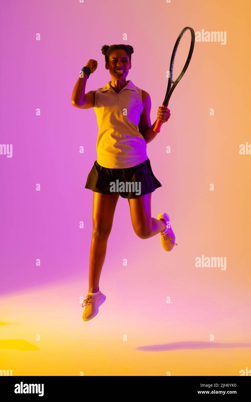 Image verticale d'une joueuse de tennis afro-américaine réussie dans un éclairage violet et jaune Banque D'Images