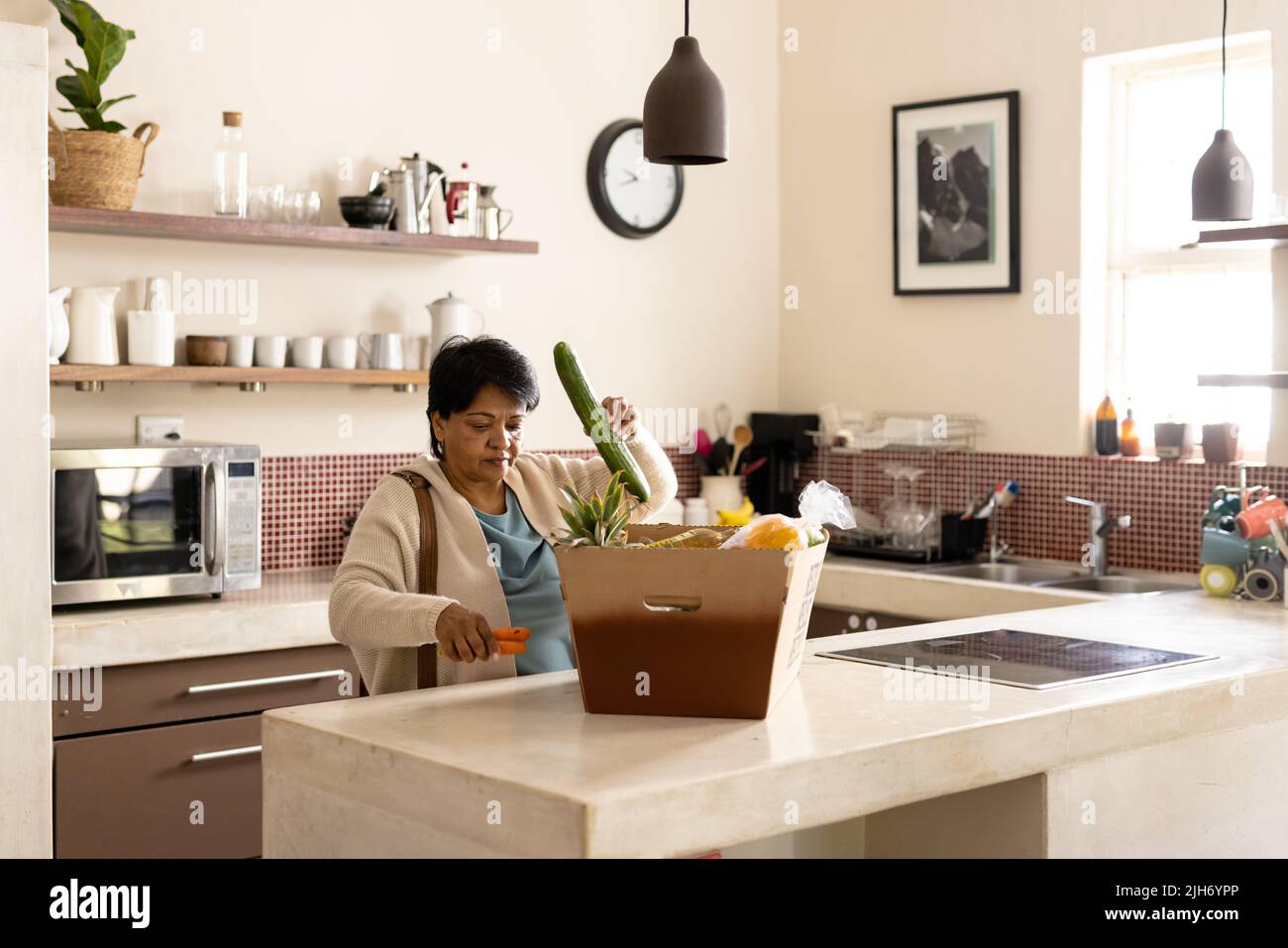 Biracial mature femme avec les cheveux courts déballer les produits frais de la boîte en carton sur l'île de cuisine Banque D'Images