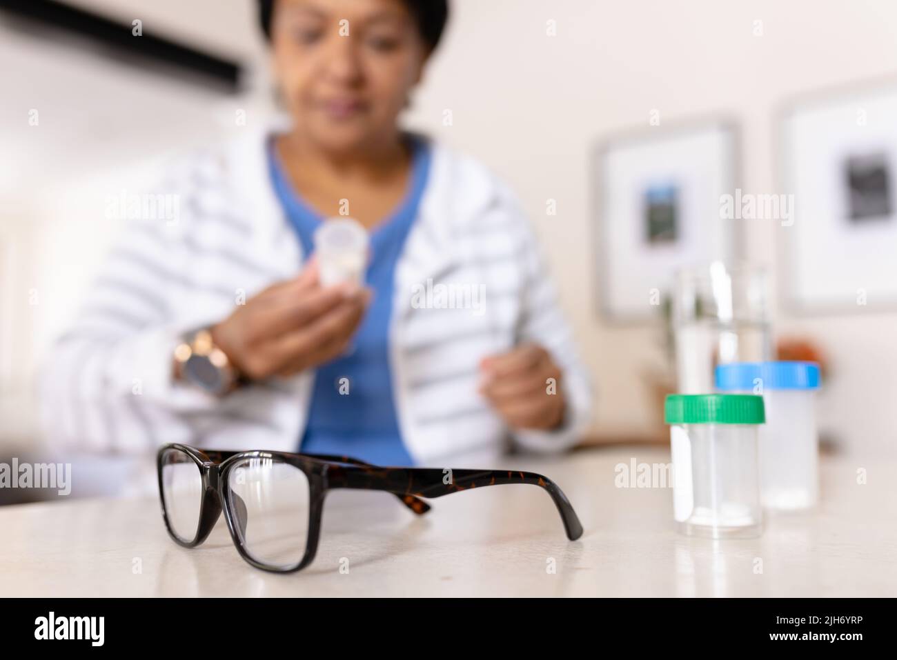 Femme biraciale mature avec lunettes et bouteilles de médicaments sur table à la maison Banque D'Images