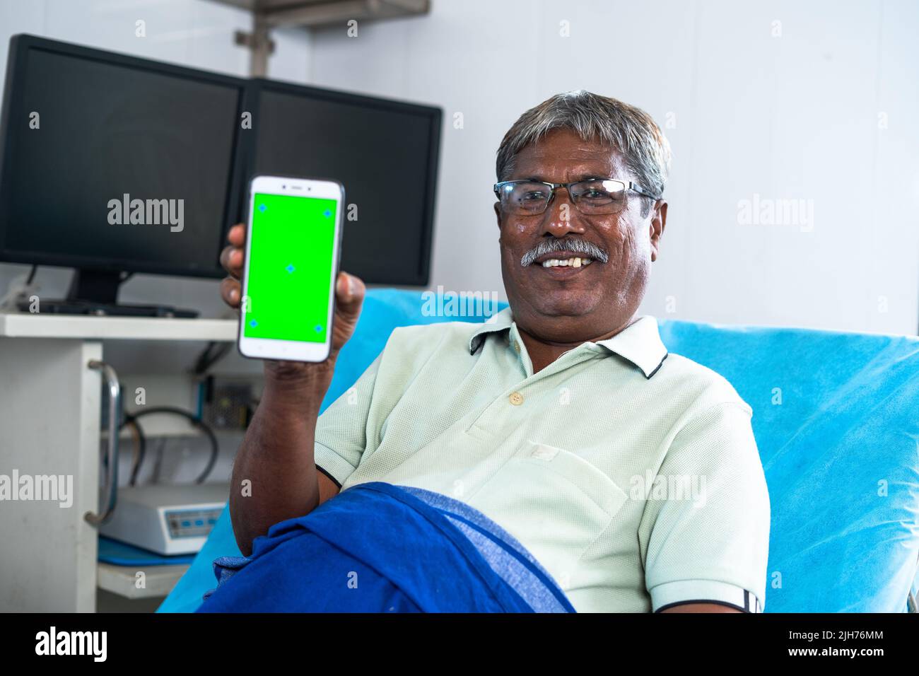 Heureux patient souriant montrant le téléphone mobile à écran vert en regardant la caméra pendant le sommeil sur le lit à l'hôpital - concept de service de santé Banque D'Images