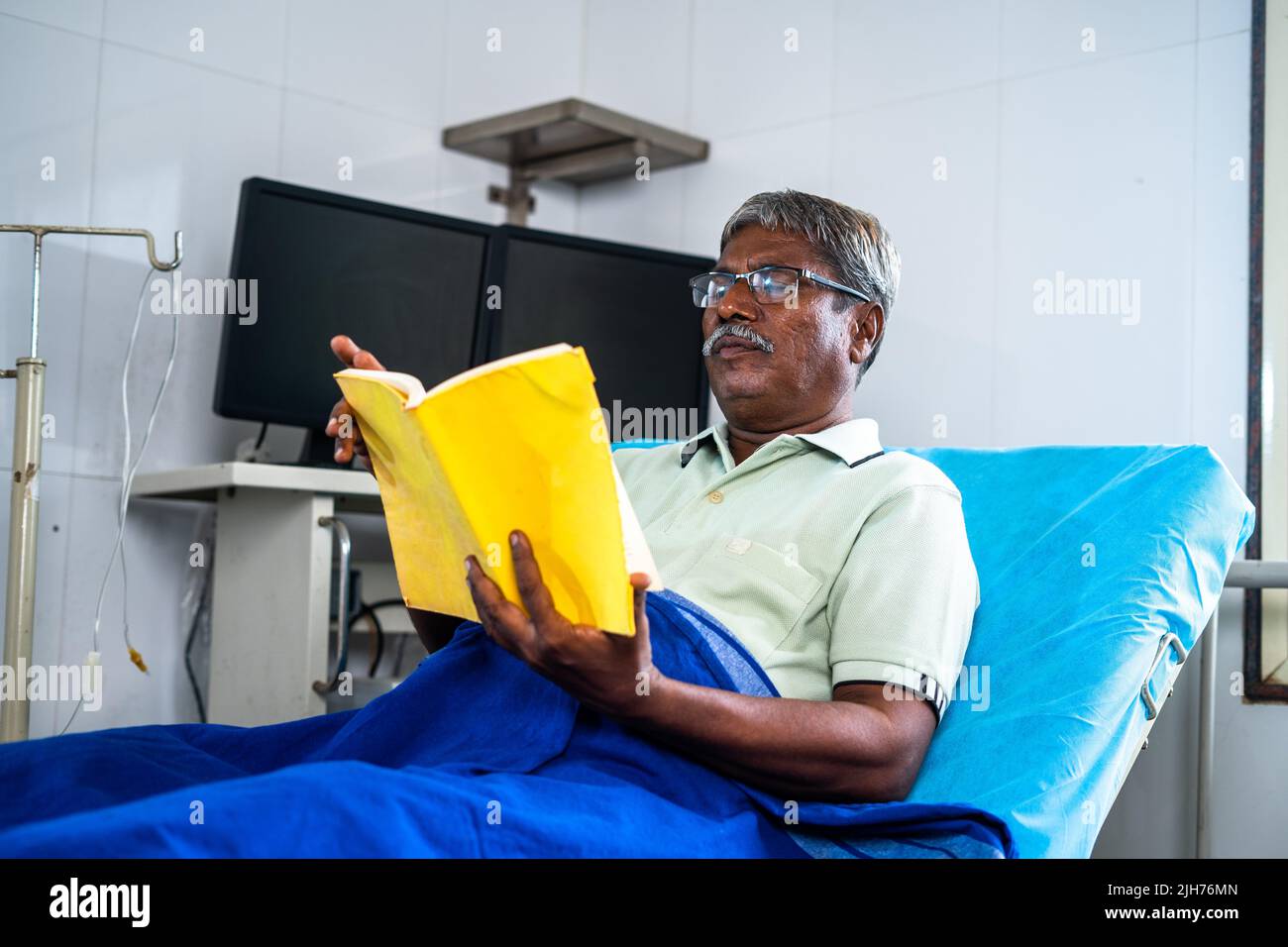 Homme âgé avec livre de lecture de lunettes à l'hôpital pendant le lit - concept de relaxation, de réadaptation et de traitement d'assurance-maladie. Banque D'Images