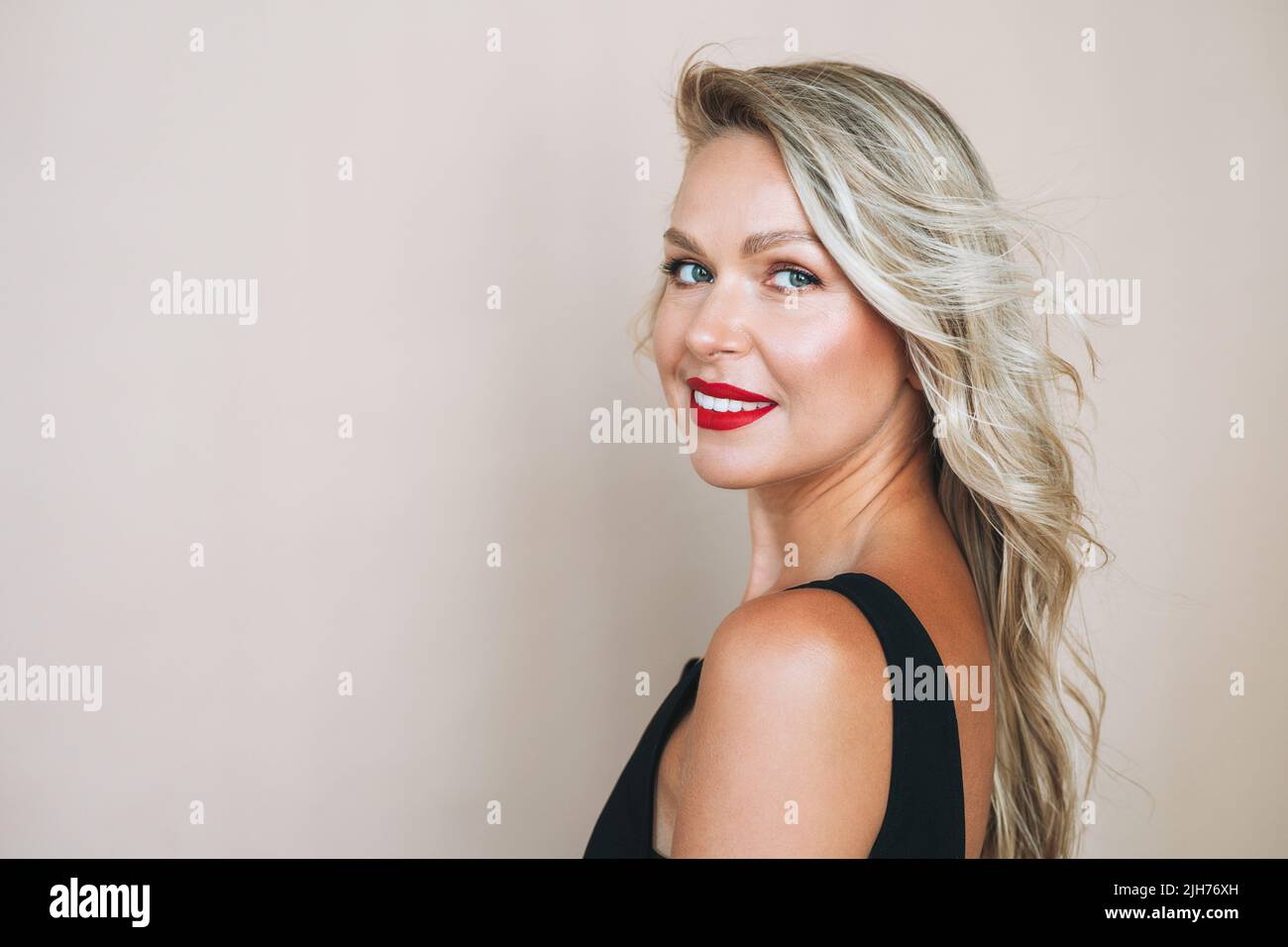 Portrait d'une magnifique blonde heureuse jeune femme avec un maquillage brillant en robe de soirée sur fond beige Banque D'Images