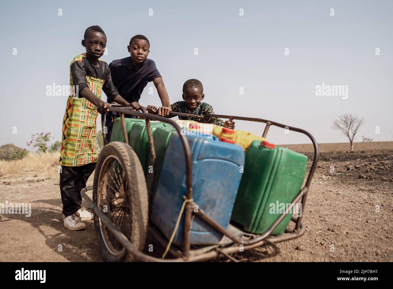 Groupe de jeunes garçons africains poussant un chariot lourd plein de bidons d'eau; manque d'approvisionnement en eau domestique dans les pays en développement Banque D'Images